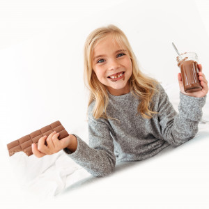 Cute funny girl holding chocolate bar and showing her dirty teeth, looking at camera